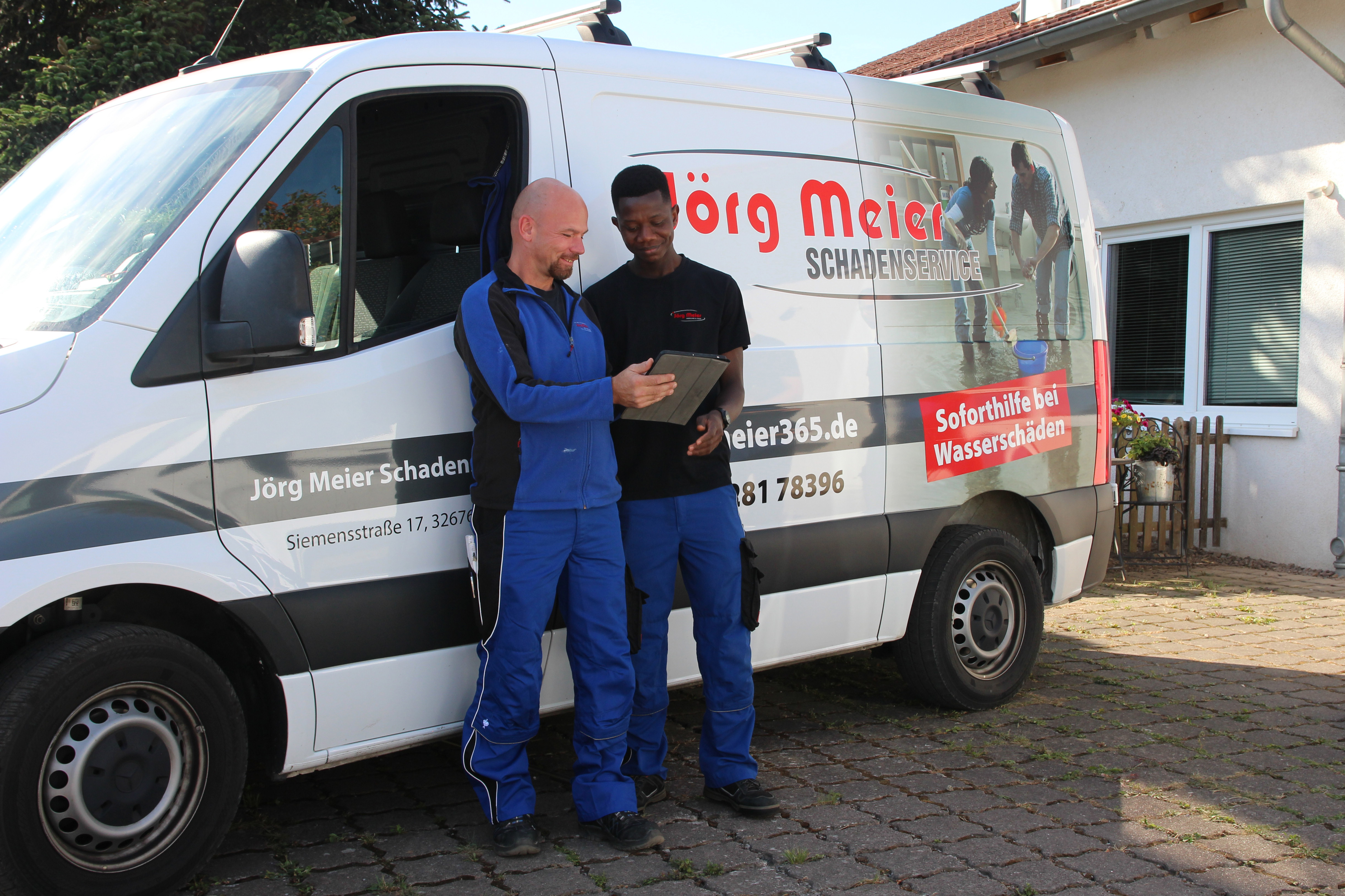 Zwei Mitarbeiter stehen vor einem Firmenbulli und schauen auf ein Tablet