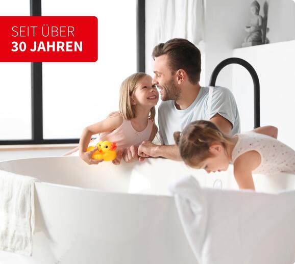 Vater spielt mit seinen zwei Kindern an einer freistehenden Badewanne