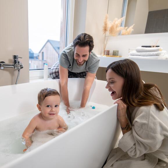 Familie sitzt im Bad um eine freistehende Badewanne